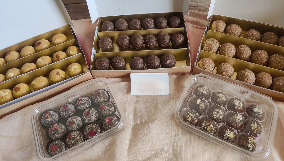 An assortment of laddoo boxes with coconut and rose-topped laddoos